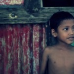 A young boy waits for his mother outside their village home.